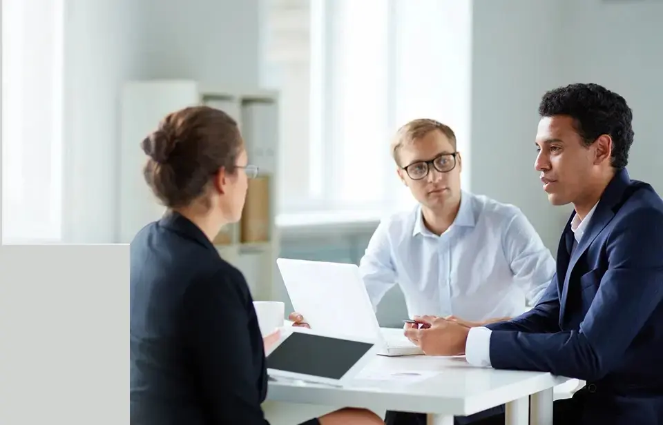 Three people sitting at a table with one man holding a laptop.